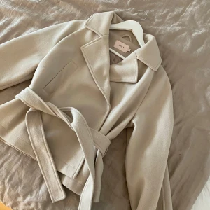 Beige kappa med bälte från Nelly - Jätte fin jacka/kappa ifrån Nelly. Passar perfekt till hösten och våren. Har knappt använt den, så den är i ett väldigt fint skick. Passade inte riktigt på mig så har bara hängt i garderoben tyvärr. Hoppas den kan komma till användning utav någon annan🥰Köpt för 699kr, förra året ifrån Nelly.com 
