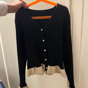 Svart ribbad kofta med beige volang - Supersöt svart ribbad kofta med v-ringning och knappar.