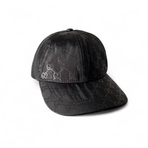 Svart Gucci keps med GG-mönster - Snygg svart keps från Gucci med klassiskt GG-mönster över hela framsidan och skärmen. Baksidan är i mesh för extra ventilation och cool look. Perfekt för dig som vill ha en exklusiv och trendig accessoar med streetkänsla.