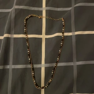 Svart och guldigt pärlhalsband - Snyggt halsband med svarta och guldiga pärlor, varvat med små silverfärgade detaljer. Kedjan är tunn och har justerbar längd med en enkel låsning. Perfekt för att ge din outfit lite extra edge och stil.