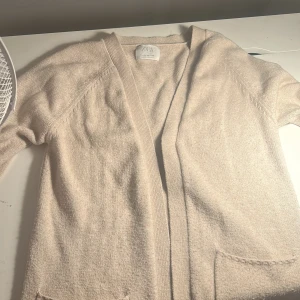 Beige kofta från Zara med fickor - Mysig beige kofta från Zara med långa ärmar och två stora fickor framtill. Koftan är stickad och har ribbade muddar vid ärmslut och nederkant. Perfekt att slänga på sig när det är lite kyligt ute.