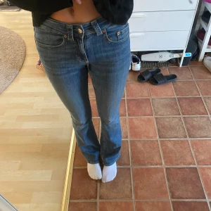 Blå bootcut jeans  - Säljer ett par klassiska blå jeans med bootcut passform. Jeansen har fem fickor, snygga detaljer med nitar och knappar, samt normal midja. Perfekta för dig som gillar en tidlös och avslappnad stil.