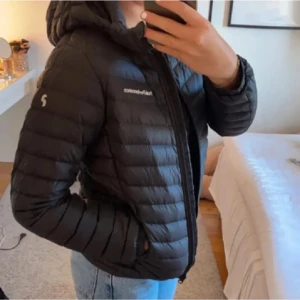 Svart dunjacka Peak Performance XS - Snygg svart dunjacka från Peak Performance i storlek XS. Jackan har huva, dragkedja och quiltad design. Perfekt för kalla dagar och har en stilren look med diskret logga på bröstet och ärmen. Materialet är lätt och smidigt, tillverkat i dun. Ett litet hål vid handen som inte syns men är där hör av er för bild 