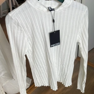 Vit ribbad långärmad tröja Pieces - Säljer en fräsch vit ribbad långärmad tröja från Pieces i storlek XS. Tröjan har en högre rund hals och är tillverkad i ett mjukt, stretchigt material. Nypris 230 kr 