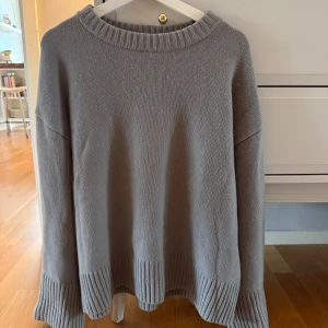 Grå stickad tröja från H&M i ull/kashmir - Mysig grå stickad tröja från H&M i en blandning av ull och kashmir. Tröjan har breda ribbade muddar vid ärmslut och nederkant samt en rund halsringning 10% Kashmir 90% ull