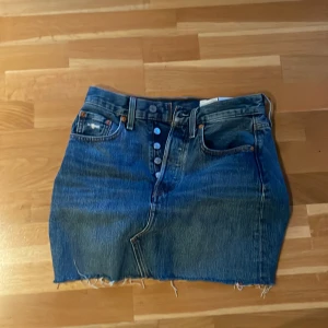 Levi's jeanskjol med rå kant - Snygg blå jeanskjol från Levi's Premium med klassiska fyra fickor , knappar framtill och rå, fransig kant nedtill. Perfekt för dig som gillar en avslappnad  stil. Tidlös denim som funkar året runt.