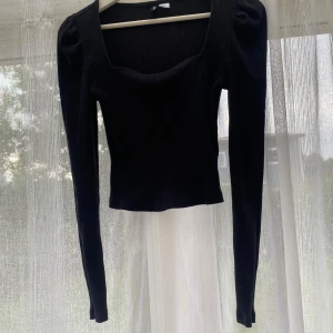Svart ribbad långärmad topp - Snygg svart ribbad topp med fyrkantig urringning och långa ärmar. Croppad modell som ger en trendig siluett, perfekt att matcha med höga jeans eller kjol. Tidlös och enkel design som passar till många olika stilar.passar S/M