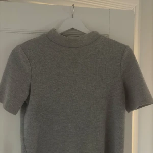 Grå polotopp från Zara Trafaluc - En stilren grå polotopp från Zara Trafaluc med korta ärmar och ribbad struktur. Toppen har en högre krage och är i ett mjukt, stretchigt material som sitter snyggt på kroppen. Perfekt att matcha med jeans eller kjol!!
