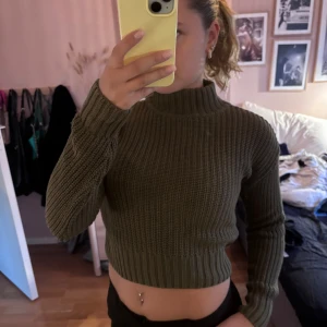 Olivgrön croppad stickad tröja Divided - Säljer en olivgrön croppad stickad tröja från Divided. Tröjan har ribbad struktur, hög hals och långa ärmar. Perfekt för lager-på-lager och snygg till både jeans och kjol. Superenkel att styla för en chill look.