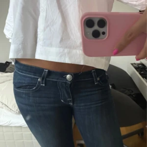 Mörkblå bootcut jeans med detaljer - Säljer ett par mörkblå bootcut jeans med låg midja och snygga vita sömmar. Bakfickorna har coola broderade detaljer i vitt. Jeansen har klassisk femficksdesign och är tillverkade i stretchigt denim för en bekväm passform. Köpte de från vinted precis men tyvärr för stora för mig. 