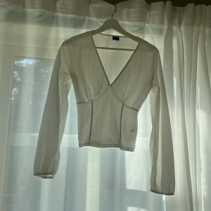 Vit omlottopp med v-ringning - Säljer en vit omlottopp med djup v-ringning och lång ärm. Toppen har en lätt ribbad struktur och sitter figurnära över kroppen. 