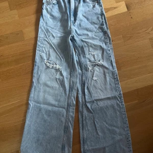 Ljusblå wide jeans från H&M Divided - Ljusblå jeans med wide fit från H&M Divided. Byxorna har hög midja, raka och vida ben samt slitna detaljer på båda benen. Tillverkade i 100% bomull.