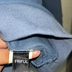 Blå fleece half zip från FRIFUL - Mysig blå fleece-tröja från FRIFUL med broderad text 'Leisure' i olika färger på bröstet. Tröjan har half zip och hög krage, perfekt för kyliga dagar. Långärmad och i mjukt fleecematerial som håller dig varm och bekväm.