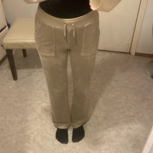 Beige juicy byxor  - Säljer ett par beige mjukisbyxor med raka ben och bred resår i midjan. Byxorna har snörning framtill, stora fickor fram och en extra ficka på sidan. Mjukt material som känns skönt mot huden, perfekta för chill dagar.