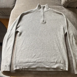 Grå half zip tröja från Lindex - Säljer en stilren grå långärmad tröja från Lindex med half zip och hög krage. Tröjan är ribbstickad och har en klassisk passform som funkar till många outfits. Perfekt för kyligare dagar och enkel att matcha. Väldigt skön passform