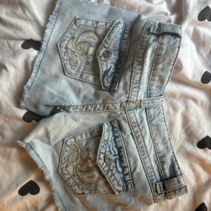 Ljusblå jeansshorts från Gina Tricot - Snygga ljusblå jeansshorts från Gina Tricot med fransiga kanter och cool broderad detalj på bakfickorna. Shortsen har klassisk femficksdesign, knappstängning och bälteshällor. Perfekta för sommarens alla äventyr!