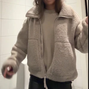 Beige teddyjacka med dragkedja - Mysig beige teddyjacka med oversized passform och stora fickor framtill. Jackan har hög krage och stängs med dragkedja. Perfekt för kalla dagar när du vill vara både varm och snygg.
