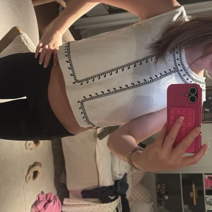 Vit broderad linnetopp från MNG - Superfin vit linnetopp från MNG med svart broderad detalj runt halsen och längs framsidan. Toppen är ärmlös och croppad, perfekt till jeans eller kjol. Sval och luftig med snyggt mönster som ger en boho-vibe.