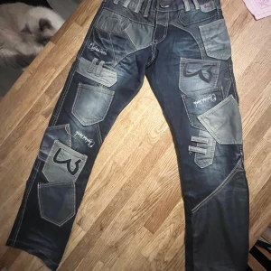 Japrag denim jeans med patchwork - Unika mörkblå denim jeans från Japrag med gråa patchwork-detaljer och broderade fickor. Snygga kontrastsömmar, flera fickor och coola applikationer ger ett streetwear-inspirerat uttryck. Perfekta för dig som vill sticka ut med din stil. 41cm bredd, 99cm längd