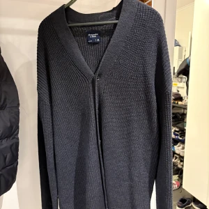 Svart kofta från Abercrombie & Fitch - Säljer en svart, stickad kofta från Abercrombie & Fitch i storlek M men sitter som L. Koftan har v-ringning, lång ärm och en enkel knapp framtill. Perfekt att slänga på sig när det är lite kyligare ute. Stilren och enkel design som funkar till det mesta. 