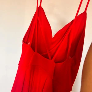 Röd långklänning med smala axelband - Säljer en röd klänning med smala axelband och v-ringad front. Klänningen har en stilren och elegant siluett med mjukt fallande tyg. Perfekt för dig som vill sticka ut med en färgstark look. Materialet känns lätt och följsamt mot kroppen.