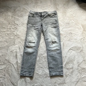 Grå ripped jeans Supply & Demand - Snygga grå jeans från Supply & Demand med slitna detaljer och hål på knäna för en edgy look. Modellen har fem fickor, knapp och dragkedja framtill samt raka ben. Perfekt för dig som gillar streetstyle och vill sticka ut.