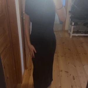 Mörkblå långklänning med kort ärm - Säljer en mörkblå långklänning med korta ärmar och figurnära passform. Knappt använd och är i bra skick. Är 158 lång och den passar perfekt i längden. Den är i en jätte mörkblå färg och ser därför svart ut i bilden. 