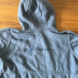 Grå hoodie från Hoodrich XL - Säljer en grå hoodie från Hoodrich i storlek XL för tonåringar. Tröjan har tryck med Hoodrich-logga på bröstet och coolt statement på ryggen. Klassisk känguruficka framtill och huva. Perfekt för streetwear-stilen och chill dagar.