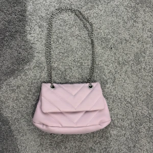 Ljuslila quiltad axelväska med kedja - Säljer en ljuslila quiltad axelväska. Som går att ha kort eller långt kedjerem, med silverfärgad kedjerem. Väskan har ett lock med magnetlås.