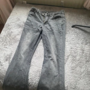 Grå jeans med råa benslut - Säljer ett par grå jeans med snyggt slitna detaljer och råa, avklippta benslut. Klassisk femficksmodell med dragkedja och knapp framtill. Jeansen har en rak passform och är tillverkade i mjukt denimtyg. Perfekta för en avslappnad streetstil.