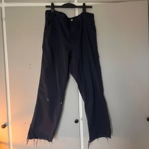 Mörkblå Carhartt Simple Pant - Mörkblå byxor från Carhartt med raka ben och råa, fransiga benslut. Klassisk workwear-look med bakfickor och Carhartt-logga. Tillverkade i slitstark bomull, loose fit och perfekt för dig som gillar streetwear vibes.