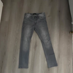 Slim fit grå jeans Glenn  - Snygga grå slim fit jeans från Glenn i storlek 30/32. Jeansen har klassisk femficksdesign, raka ben och en tvättad look med ljusare partier. Perfekta för dig som gillar en stilren och modern vibe.