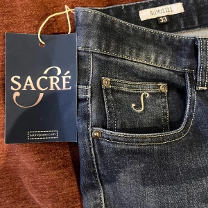 Slim fit jeans från Sacré, blå w33 helt nya! - Nya med tags kvar. Snygga slim fit jeans från Sacré i klassisk blå tvätt med diskreta slitningar och kontrastsömmar. Jeansen har fem fickor, silverfärgade nitar och en liten broderad S på myntfickan. Perfekta för dig som gillar en modern och stilren look. Innerbenslängd ca 80 cm.