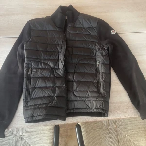 Svart M⭐️ncler pufferjacka med stickade ärmar - Snygg svart pufferjacka från M⭐️ncler med quiltad framsida och stickade ärmar och rygg. Jackan har dragkedja framtill, två dragkedjefickor och klassisk Moncler-logga på ena ärmen. Perfekt för dig som vill ha en stilren och sportig look. Proset ör inte satt än utan har bara skrivit dit några siffer så de gör att diskuteras!!