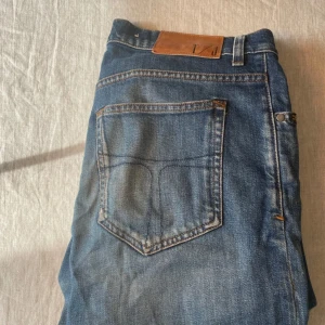 Blå jeans från Tiger of Sweden, Evolve - Snygga blå jeans från Tiger of Sweden i modellen Evolve. Klassisk femficksdesign, läderpatch med logga bak och kontrastsömmar. Jeansen har en rak passform och är tillverkade i slitstarkt denimtyg. Perfekta för en stilren och avslappnad look.