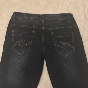 Mörkblå Goody jeans med broderade fickor - Snygga mörkblå jeans från Goody jeans med kontrastsömmar och broderade detaljer på bakfickorna. Klassisk femficksmodell med raka ben och normal passform. Jeansen har en lätt tvättad look och är tillverkade i slitstarkt denimtyg.
