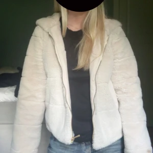 Beige teddyjacka med huva - Supermjuk och fluffig beige teddyjacka med dragkedja och stor huva. Jackan har en avslappnad passform och är perfekt för kyliga dagar. Fodrad insida för extra komfort och värme. Enkel att matcha med jeans eller leggings för en chill look.