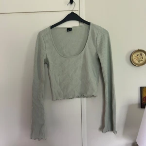 Grön våffelstickad topp - Superfin grön topp från Gina Tricot med lång ärm och våffelstickat material. Toppen har en djup rundad urringning och vågig kant nertill och vid ärmslut. 