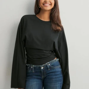 Svart långärmad tröja med vida ärmar - En svart långärmad tröja med rund hals och extra vida ärmar. Tröjan har en tightare passform i midjan och är tillverkad i ett mjukt material som känns skönt mot huden. Perfekt för dig som gillar en stilren och enkel look.