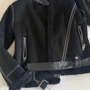 Svart teddyjacka från Zara - Säljer en svart teddyjacka från Zara med jättefina detaljer och dragkedjor samt bälte. Perfekt för kalla dagar. Mjuk och fluffig på insidan.