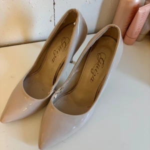 Beige pumps med spetsig tå från Chilla - Snygga beige pumps från Chilla med glansig finish och spetsig tå. Skorna har hög klack och en klassisk siluett som ger en elegant look. Perfekta för dig som gillar stilrena och feminina skor med lite extra höjd.