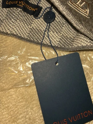 Grå rutig Louis Vuitton väst - Säljer en grå väst från Louis Vuitton med klassiskt rutigt mönster och LV-logga broderad på bröstet. Västen är stickad och har en snygg, mörkgrå ton. Perfekt för dig som vill ha något exklusivt och stilrent i garderoben.