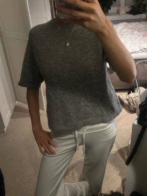 Grå stickad kortärmad tröja - Mysig grå stickad tröja med korta ärmar och rund hals. Tröjan har en loose passform och är perfekt för lager-på-lager under kyliga dagar. Materialet känns mjukt och skönt mot huden, och den neutrala färgen gör den enkel att matcha med olika outfits.