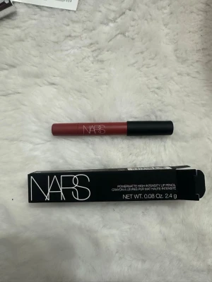 NARS Powermatte Lip Pencil - NARS Powermatte High-Intensity Lip Pencil i en snygg rödrosa nyans. Pennan har en matt finish och kommer i en smidig, tunn form med svart lock. Perfekt för att skapa definierade och intensiva läppar. Innehåller 2,4 g.