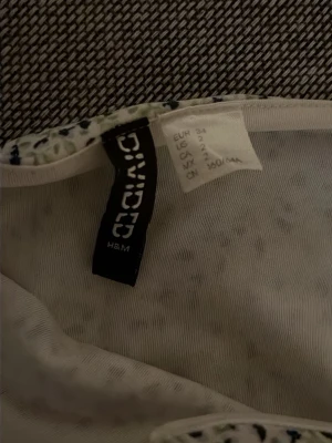 Kjol från H&M - En vit/blå/grön blommig kort kjol. Från H&M. Med dragkedja i sidan. Storlek 34.