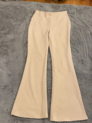 Beiga bootcut byxor med hög midja - Snygga beiga bootcut-byxor med hög midja och utsvängda ben. Byxorna har en stilren design utan synliga detaljer och är gjorda i ett mjukt material som känns skönt mot huden. Perfekta för dig som gillar en trendig och avslappnad look .Kan eventuellt tänka mig gå ner i pris