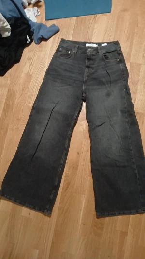 Svarta wide jeans med raka ben - Säljer ett par svarta jeans med breda, raka ben och klassisk femficksdesign. Jeansen har en mörk tvätt och är tillverkade i robust denim. Baktill finns två stora fickor och en enkel söm. Perfekt för dig som gillar loose fit och avslappnad stil.