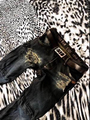 G-Star Raw Ripped Denim - Säljer ett par svarta jeans från G-Star Raw med slitna detaljer och coola revor framtill. Byxorna har raka ben, klassiska fickor och medföljande svart bälte med metallspänne. Perfekt för dig som gillar streetstyle och vill sticka ut.