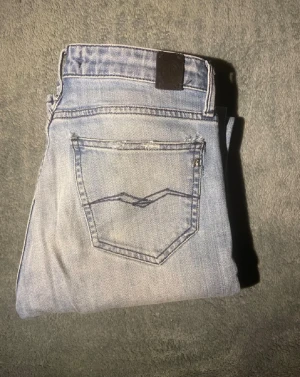 Replay ljusa jeans, storlek 27/32 - Säljer ett par ljusblå jeans från Replay med klassisk femficksdesign och snygga detaljer på bakfickan. Jeansen har normal passform och raka ben, tillverkade i mjukt denim-material. Perfekt för dig som gillar stilrena och bekväma jeans.