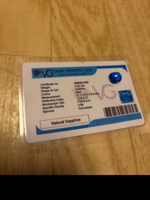 Blå safirväst med cushion cut - Säljer en blå väst med cushion cut, tillverkad av naturlig safir. Västen har en intensiv blå färg och en elegant, fyrkantig form. Perfekt för dig som vill sticka ut med en unik accessoar. Storlek ca 11,7 x 8,2 x 5,6 mm. Certifikat från VG Gems Testing Lab medföljer.